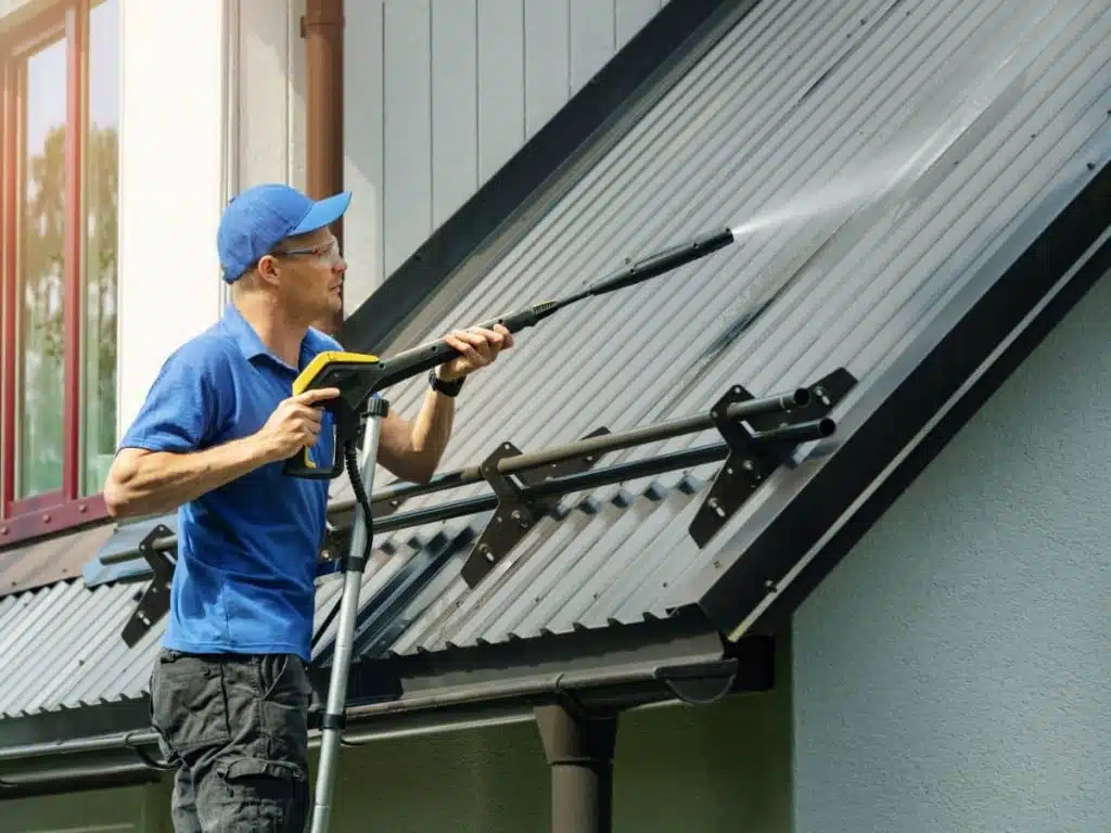 man standing on ladder and cleaning house metal roof